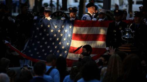 Policiais e bombeiros de Nova York seguram a bandeira dos EUA durante execução do hino nas celebrações do 11 de Setembro