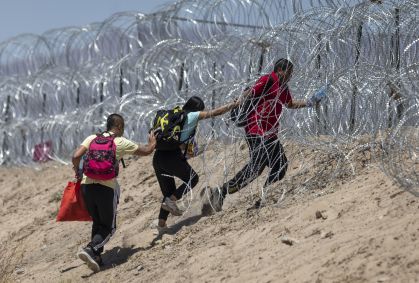 Imigrantes atravessam arame farpado em torno de um acampamento improvisado depois de cruzar a fronteira do México, em 11 de maio de 2023 em El Paso, Texas