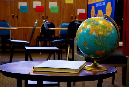 Sala de aula. Há um globo terrestre e um caderno em cima de uma mesa