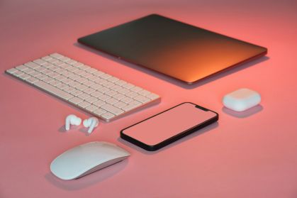 Eletrônicos em cima de mesa. Há um celular, notebook, fone de ouvido, mouse